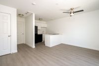 Open plan kitchen and living area with wooden floors, ceiling fan, doors, counters, cupboards, fridge, oven, and sink.
