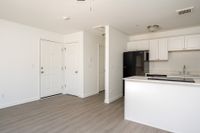Open plan living and kitchen area with doors, wooden floors, counters, fridge, sink, and oven.