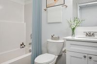 virtually staged bathroom with bath, toilet, sink, and mirror.
