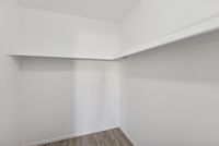 Walk-in closet with white walls and a built-in storage shelf and hanging rod.