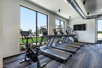 Modern fitness center with treadmills and a stationary bike, featuring expansive windows with a view of a green landscape.