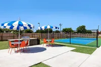 Outdoor area with blue and white umbrellas, orange chairs, and a tennis court.