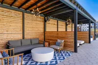 Stylish outdoor lounge area with modern seating, wooden paneling, and geometric rug under a pergola.