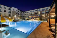 Elegant apartment complex with illuminated pool and lounge area at night.