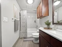 Modern bathroom featuring elegant wooden cabinetry, sleek white tiles, a spacious bathtub, and stylish vanity with greenery.