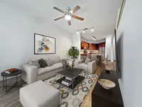 Bright and welcoming open-concept living room with elegant decor, a modern ceiling fan, and a stylish kitchen in the background.