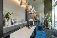 Luxurious and modern lobby with elegant decor, featuring stylish pendant lighting, a sleek white desk, vibrant blue seating, and lush greenery.