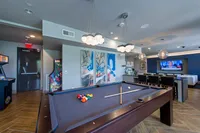 Luxury entertainment room featuring a stylish pool table, modern seating area, wall art, and arcade games under elegant lighting.