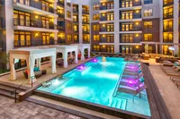 Luxurious apartment complex with a sparkling illuminated pool, elegant poolside cabanas, and modern balconies creating an inviting evening ambiance.