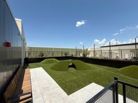 Chic rooftop garden with soft artificial grass mounds, spacious seating, and a panoramic view of clear blue skies.