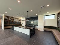 Modern kitchen and lounge area featuring sleek black countertops, pendant lighting, and stylish wood paneling.