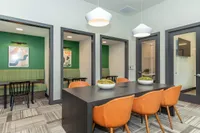 Contemporary meeting space with modern conference table, vibrant orange chairs, and cozy booths in a stylish office setting.