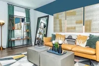 Chic living room with a cozy mustard sofa, modern artwork, and elegant decor accents. Features a stylish mirrored wardrobe and vibrant geometric rug, offering an inviting and sophisticated ambiance.