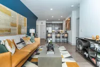 Modern living space with chic decor, featuring a stylish tan sofa with vibrant cushions, a sleek coffee table, and a cozy open-concept kitchen with bar seating.