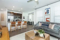 Modern living room showcasing a stylish open-concept kitchen with sleek dark cabinetry and breakfast bar seating; cozy sofa and elegant decor complete the inviting space.