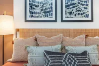 Cozy bedroom setting featuring a wicker headboard with elegant patterned pillows and abstract wall art in a warm, inviting ambiance.