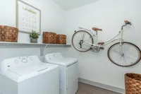 Modern laundry room with washing machine, dryer, stylish woven baskets, and a mounted vintage bicycle for chic storage.