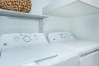 Modern laundry area with sleek white washer and dryer, accentuated by a chic woven basket on a stylish shelf.