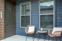 Inviting apartment entryway with stylish outdoor seating and modern blue siding, perfect for relaxation.