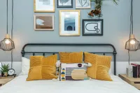 Chic bedroom with modern wall art, vibrant mustard cushions, and stylish pendant lighting, creating a cozy and artistic ambiance.