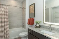 Modern bathroom featuring a stylish granite vanity, illuminated mirror, and elegant tiled shower with a chic curtain.