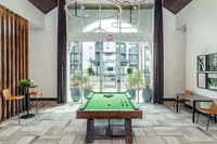 Chic apartment lounge featuring a modern pool table, elegant seating, and large windows with natural light.