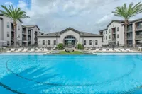 Luxurious apartment complex featuring a sparkling blue pool, surrounded by stylish lounge chairs and elegant palm trees, perfect for relaxation and leisure.