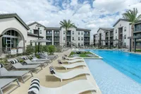 Luxurious apartment complex with a sparkling pool, stylish loungers, and elegant architecture under a blue sky.