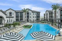 Luxurious apartment complex showcasing a pristine swimming pool surrounded by elegant lounge chairs and stylish black-and-white umbrellas, offering a resort-style living experience.