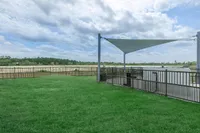 Expansive green lawn with modern fencing and shade sail, offering stunning scenic views of a vast open field under a partly cloudy sky.
