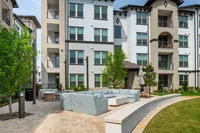 Contemporary apartment complex featuring stylish outdoor seating area with cozy couches and lush greenery.