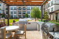 Elegant outdoor communal area with modern gas grills, stylish seating, and lush green landscaping, ideal for gatherings and relaxation.