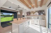 Luxurious modern kitchen with elegant marble countertops, stylish pendant lighting, and an integrated virtual golf simulator in the open-plan design.