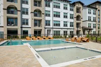 Modern apartment complex featuring a luxurious pool area with stylish lounge seating and a spacious patio.