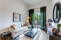 Elegant living room with chic decor, plush sofa, and glass coffee table, leading to a scenic balcony view through glass doors.