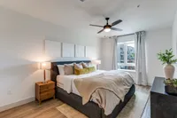 Elegant bedroom with a plush bed, stylish decor, and large window offering natural light. Modern design with contemporary art and cozy furnishings.