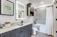 Modern bathroom with chic wooden cabinetry, illuminated mirror, and elegant bathtub in a stylish apartment setting.