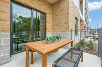Charming apartment patio with a sleek wooden table, stylish outdoor seating, and lush potted plants, perfect for relaxing under the sun.