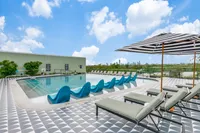 Luxurious rooftop pool area with chic lounge chairs, vibrant blue chaise lounges, and a breathtaking city skyline backdrop.