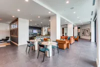 Modern apartment with open living area featuring cozy orange sofas, sleek dining tables, and a stylish kitchen with bar seating. Bright lighting and contemporary decor create an inviting atmosphere.