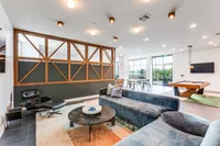 Luxurious lounge space with modern decor, plush seating, sleek pool table, and floor-to-ceiling windows opening to a vibrant outdoor view.