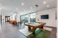 Modern recreational lounge featuring a sleek pool table, cozy seating with orange sofas, and a spacious dining area under soft lighting.