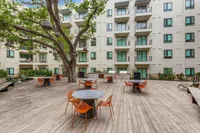 Modern apartment courtyard with stylish outdoor seating, lush greenery, and inviting communal areas under a shady tree.