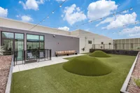 Modern rooftop terrace with lush green artificial turf, cozy seating area, and string lights under a vibrant blue sky.
