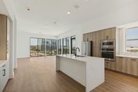 Bright open-concept apartment with sleek kitchen island, ample wood cabinetry, and floor-to-ceiling windows offering stunning city views.