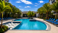 Luxurious apartment swimming pool area with elegant lounge chairs, surrounded by palm trees under a vibrant blue sky.