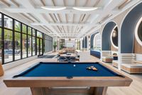 Luxurious recreational area featuring a sleek pool table, cozy seating, and expansive windows overlooking lush greenery.