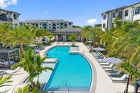 Luxurious resort-style pool area with lounge chairs and vibrant palm trees, surrounded by modern apartment buildings.