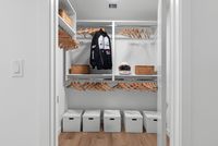 Modern walk-in closet with ample storage, featuring sleek wooden hangers, woven baskets, and stylish white storage boxes.