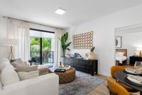 Modern living room with elegant décor, large windows allowing natural light, cozy seating, decorative plants, and a glimpse into a stylish bedroom.